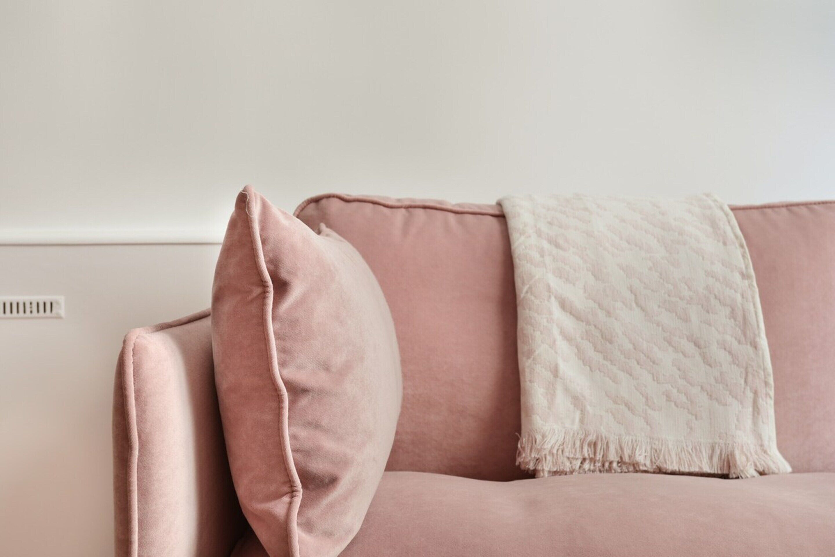 A pink sofa with a white throw blanket and a single pillow.