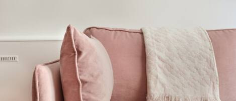 A pink sofa with a white throw blanket and a single pillow.