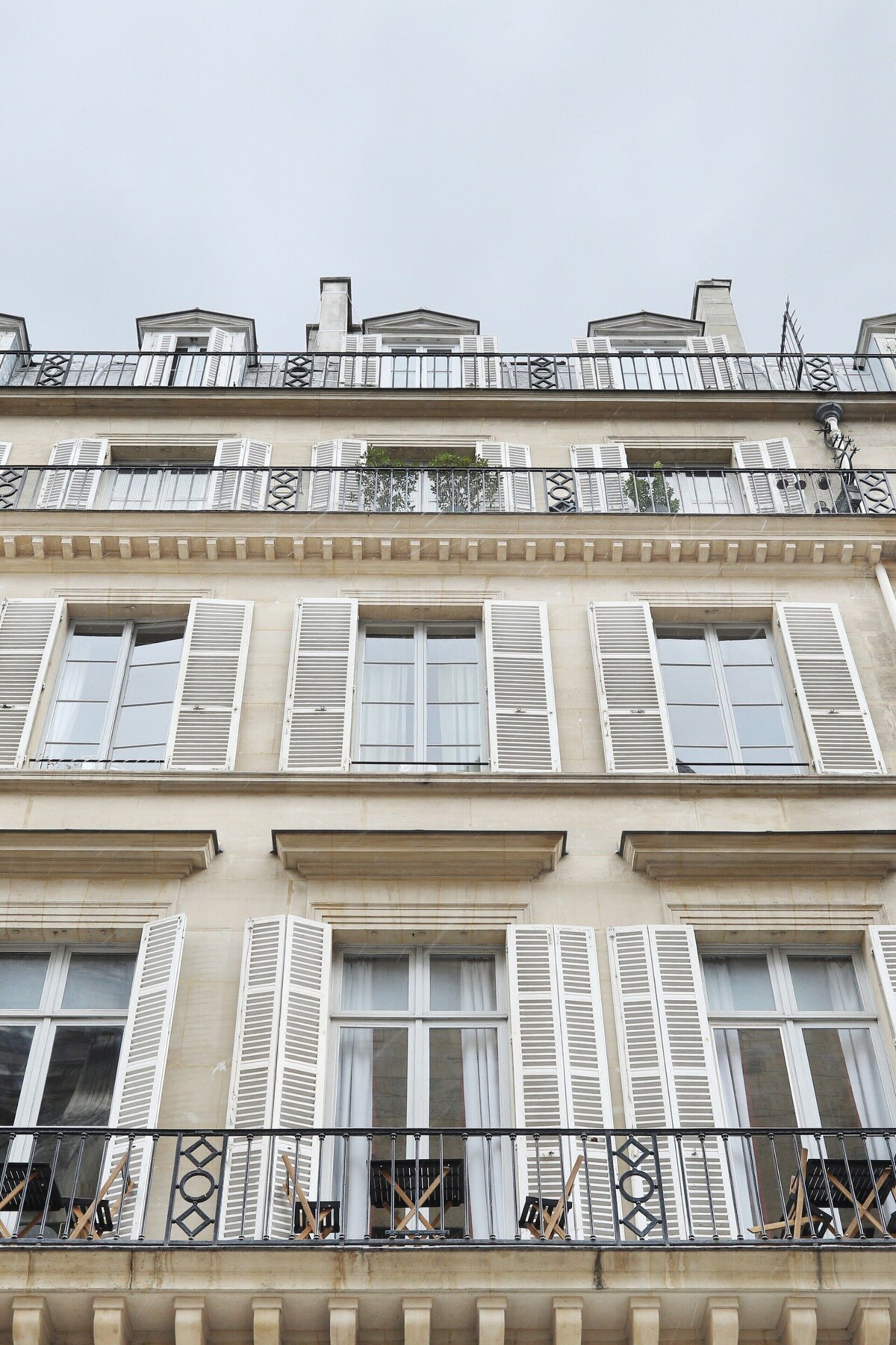 A multi-story building with white shutters on windows and balconies, featuring a classical architectural style.