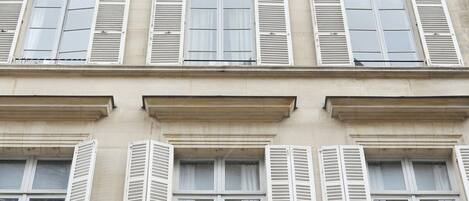 A multi-story building with white shutters on windows and balconies, featuring a classical architectural style.