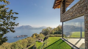 Ett modernt hus med en glasbeklädd balkong med utsikt över en sjö och berg.