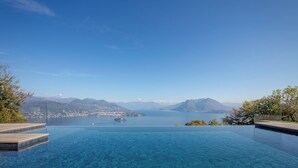 En klarblå himmel, en stor infinitypool och en utsikt över en sjö med berg i bakgrunden.