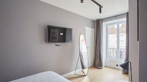 Una habitación de hotel moderna con cama, televisor de pantalla plana en la pared, espejo de pie y balcón con vistas.