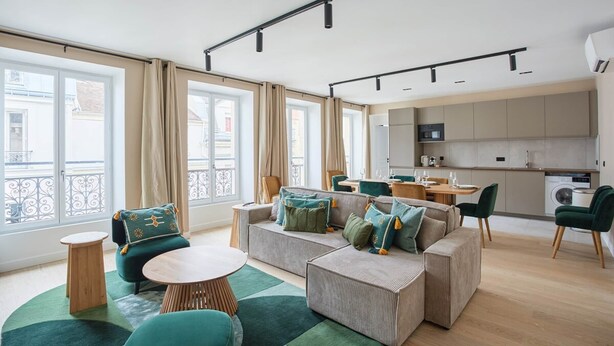 Un apartamento moderno con sala de estar, comedor y cocina. Cuenta con ventanas amplias, un conjunto de sofás y una mesa de comedor.
