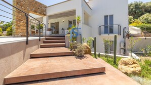 Una casa moderna amb façana de pedra, una zona exterior coberta i una escala que condueix a l'entrada.