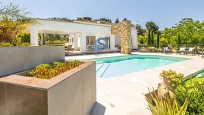 Zona de piscina moderna amb una estructura de pedra, gandules i cel blau.