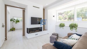 Un saló modern amb una llar de foc, televisió i una finestra gran amb plantes.