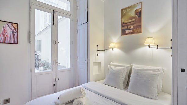 Quarto de hotel com uma cama, duas luminárias fixadas na parede, um pôster e uma janela com vista para o exterior.