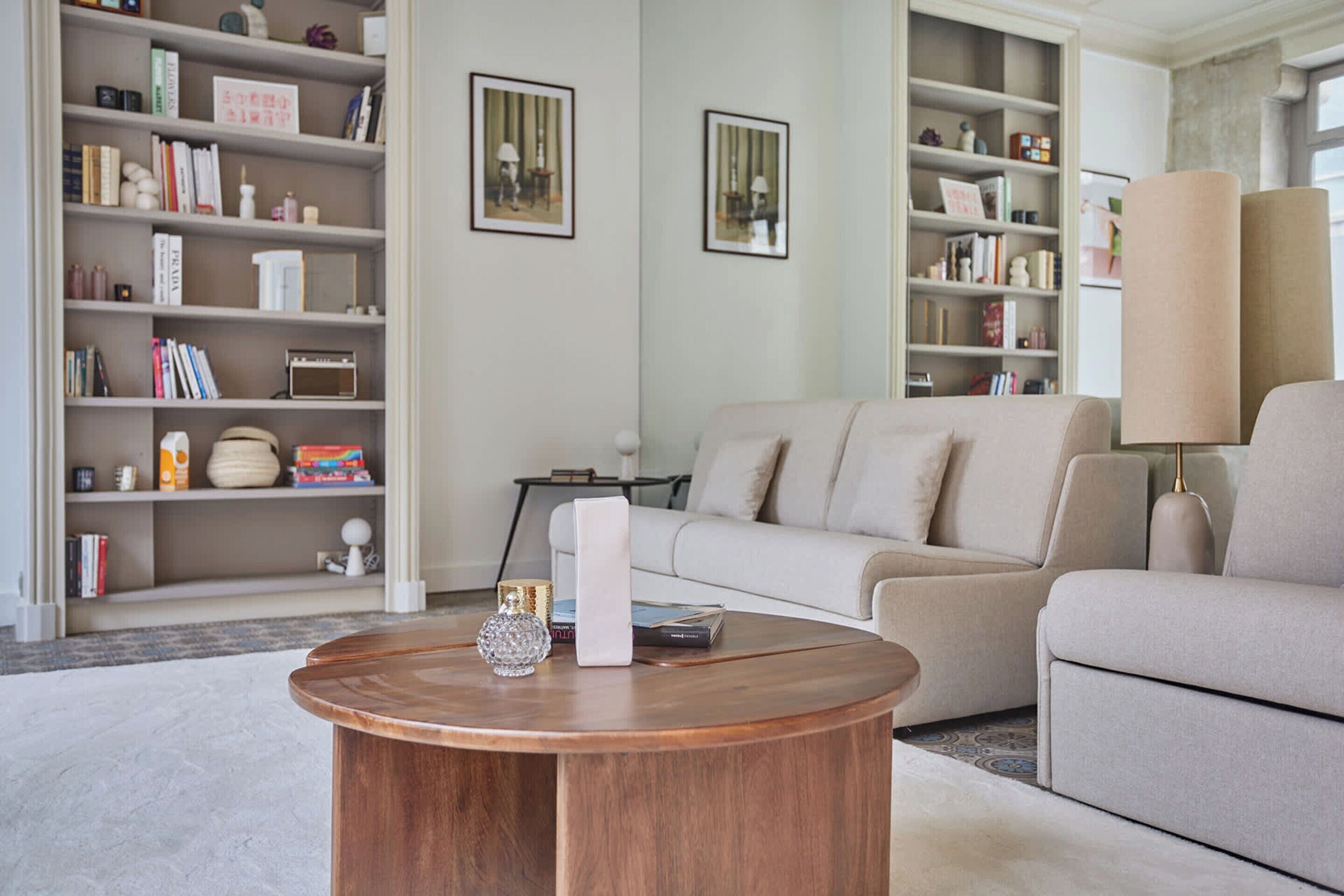 A modern living room with a beige sofa, a wooden coffee table, and a bookshelf filled with books and decorative items.