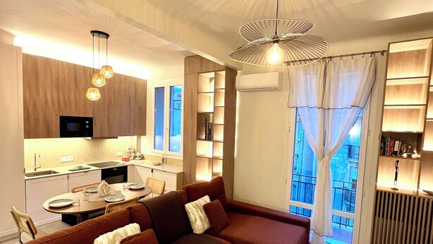 Una sala de estar moderna con un sofá seccional, una mesa de comedor y una cocina al fondo.
