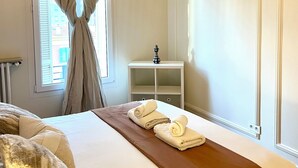 Una habitación de hotel con cama, mesita de noche, lámpara y ventana con cortinas.