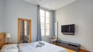 Une chambre d’hôtel avec un lit, une télévision, une chaise, un bureau et une fenêtre avec des rideaux.
