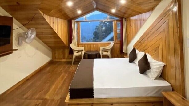 Ein gemütliches Schlafzimmer in einer Holzhütte mit einem Bett, einem kleinen Tisch, zwei Stühlen und einem Fenster mit Blick.