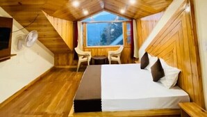 Ein gemütliches Cabin-Zimmer mit Holzbalkendecke, einem Bett mit Kissen, einem kleinen Tisch, zwei Stühlen und einem Fenster mit Aussicht.
