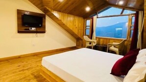 Ein Zimmer mit Holzbalkendecke, einem Bett, einem an der Wand befestigten Fernseher und einem Fenster mit Blick.
