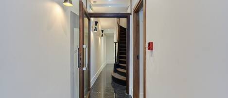 A hallway with a polished black floor, a wooden staircase, and a wall-mounted light fixture.