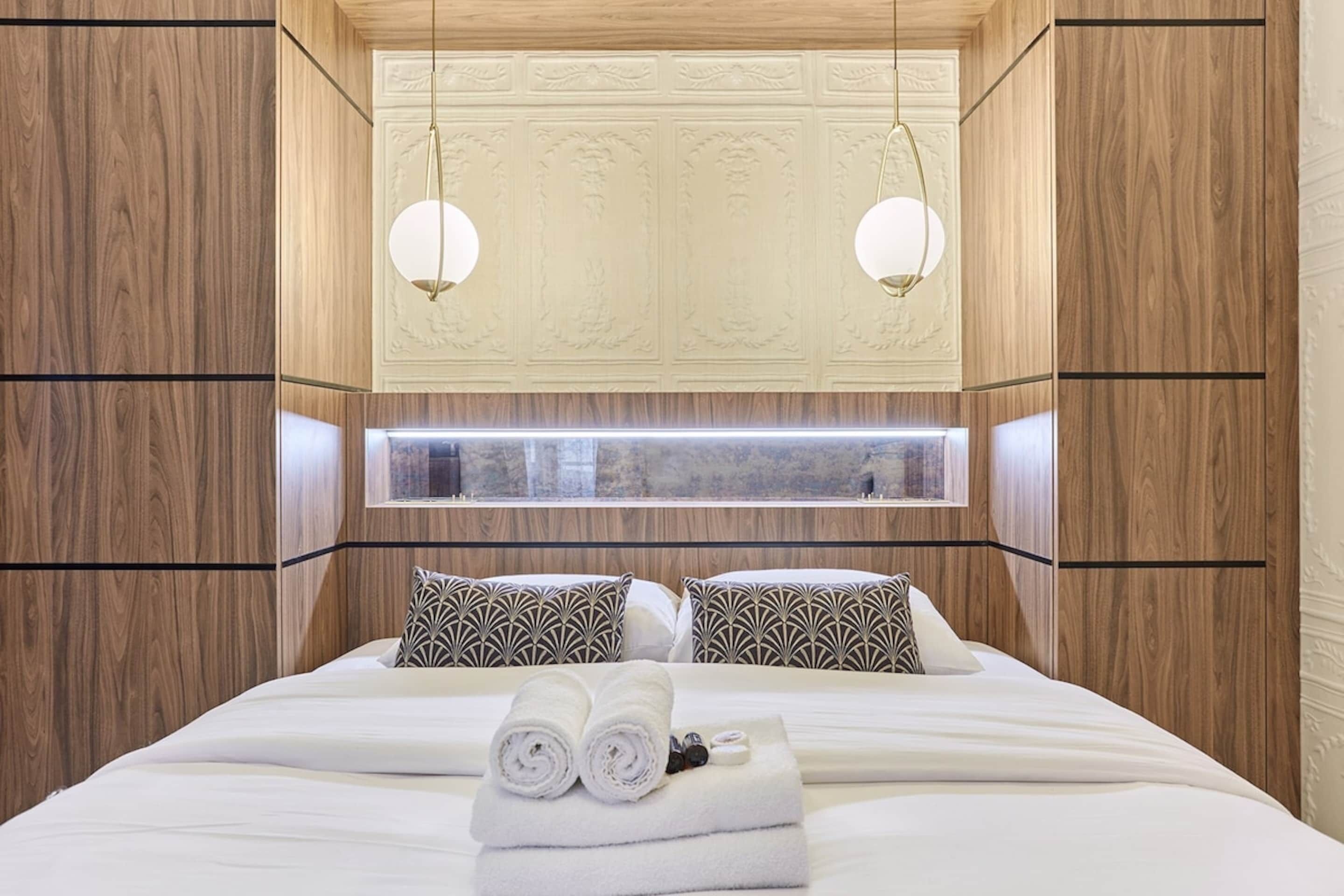 Ein Hotelzimmer mit einem großen Bett, zwei gemusterten Kissen, einem Fenster und einer Wandgestaltung aus Holz.