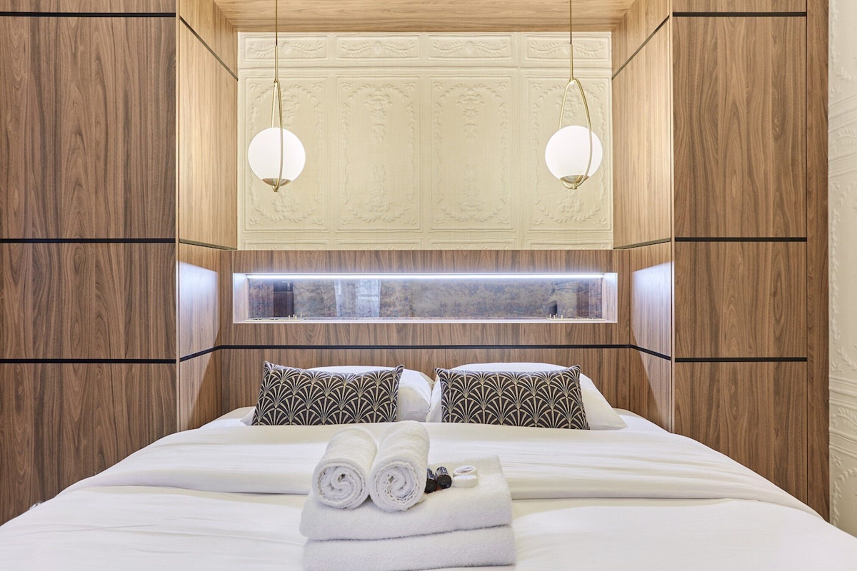 A hotel room with a large bed, two patterned pillows, a neatly made bed with towels, and a window with a view.
