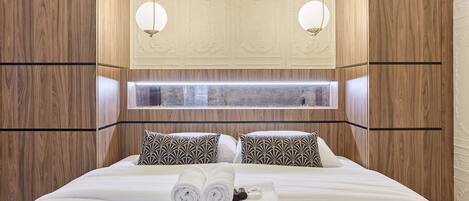 A hotel room with a large bed, two patterned pillows, a neatly made bed with towels, and a window with a view.