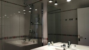 A modern bathroom with two sinks, a glass shower enclosure, and a large mirror.