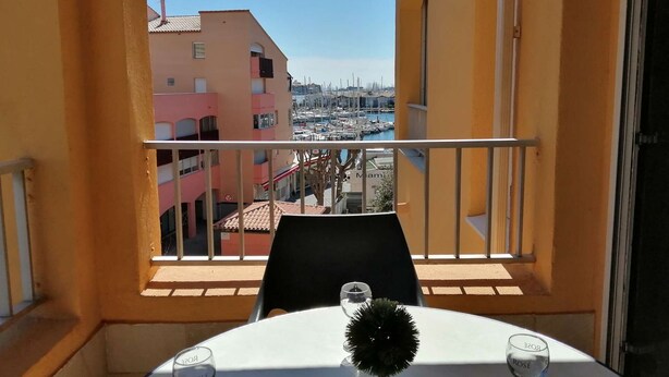 A balcony with a table set for two, overlooking a marina with boats and buildings.