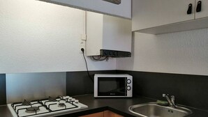 A compact kitchen with a gas stove, a microwave, a sink, and wooden cabinets.