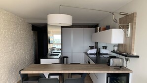 A modern kitchen with a wooden island, bar stools, a hanging light, and built-in appliances.