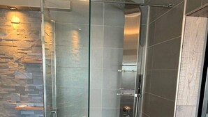 A modern shower with a glass door, a stone wall, and a tiled floor.