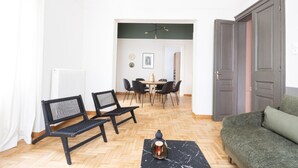 Olohuone, jossa on sohva, kaksi mustaa tuolia, ruokapöytä tuoleineen, patteri ja ovi.