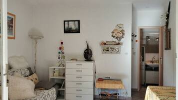 Una sala de estar con sofá, una mesita con mantel, aparador, lámpara de pie e imagen colgada en la pared.