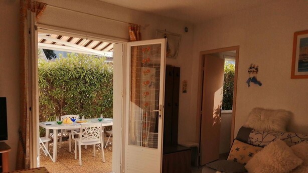 A room with a dining area, a sofa, and a door leading outside. - 2 Bed apartment ground floor / Mont St Martin (CAP D AGDE)