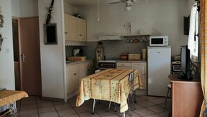 A compact kitchen with a dining table, a ceiling fan, and basic appliances. - 2 Bed apartment ground floor / Mont St Martin (CAP D AGDE)