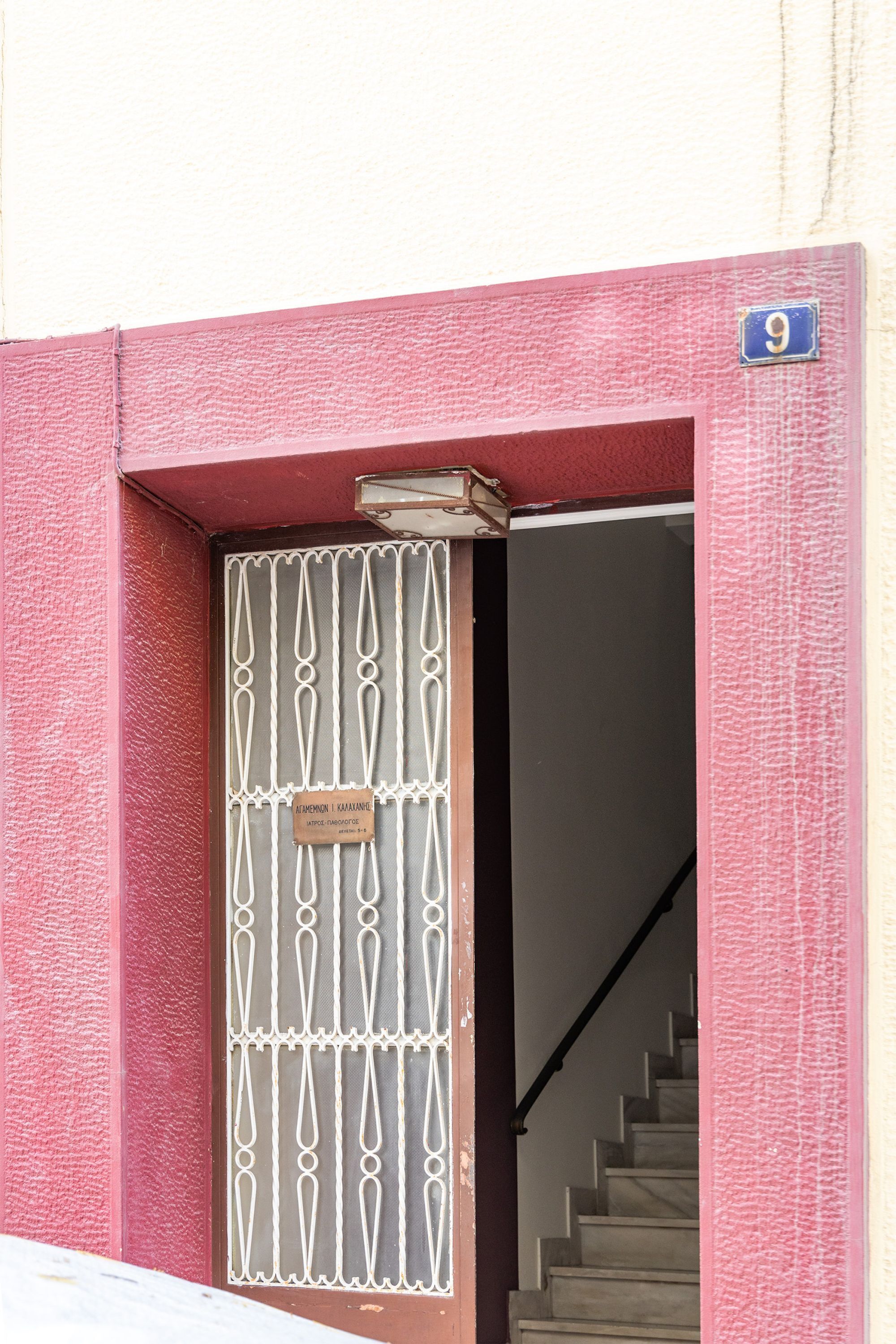A building entrance with a metal gate, a staircase, and a blue house number sign.