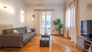 A modern living room with a grey sofa, a black marble coffee table, wooden flooring, a TV, and a potted plant. - Acropolis View 3-bdrm With Rooftop Garden Jacuzzi (Athens)