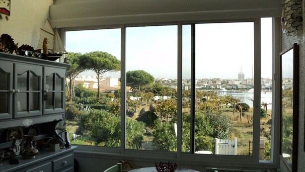 A room with a large window offering a view of a cityscape and greenery. - 1 bed + gallery apartment / Ile des Marinas (CAP D'AGDE)