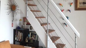 A staircase with a white railing and wooden steps, surrounded by various wall decorations including framed pictures and colorful bird figures. - 1 bed + gallery apartment / Ile des Marinas (CAP D'AGDE)