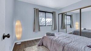A bedroom with a large mirror, a bed with a grey duvet, a fluffy rug, and a window with curtains. - 3-bedroom Artist Oasis in the HeART of Las Vegas (Las Vegas)