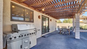 An outdoor kitchen with a grill, a dining table with chairs, and a pergola overhead. - 3-bedroom Artist Oasis in the HeART of Las Vegas (Las Vegas)