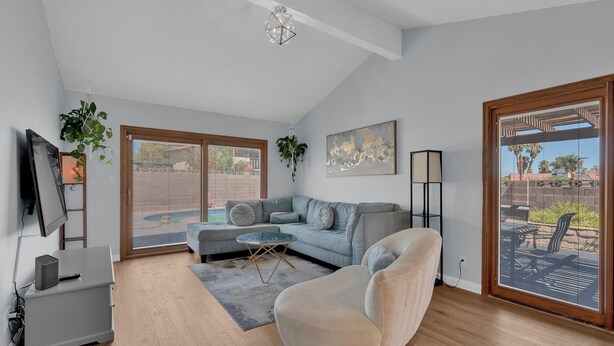 A modern living room with a grey sofa, a beige armchair, a coffee table, and a TV on a stand. There is a large window with a view of the outside. - 3-bedroom Artist Oasis in the HeART of Las Vegas (Las Vegas)