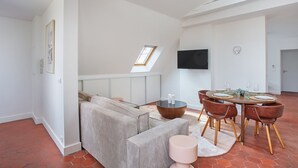 A modern living room with a sofa, a dining table with chairs, a TV mounted on the wall, and a skylight. - Superb Flat Ave Montaigne With Eiffel Tower View (Paris)