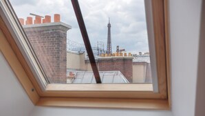 A skylight window overlooking a brick building with a tower in the distance. - Superb Flat Ave Montaigne With Eiffel Tower View (Paris)