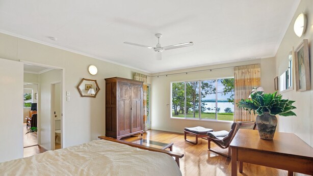 A spacious bedroom with a large bed, a wooden desk, a chair, a ceiling fan, and a view of the outdoors. - Welcome to Waterfront Views (Gympie)