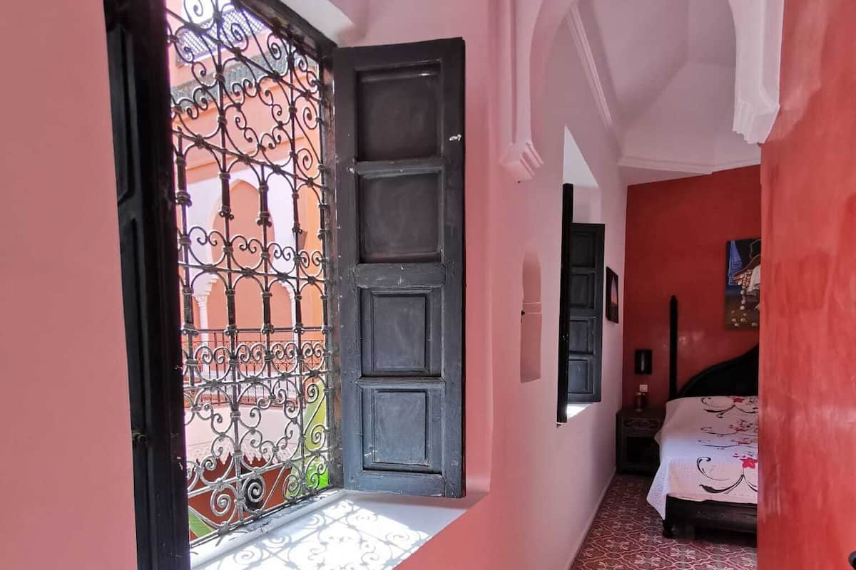 Un pasillo con piso de estampado rojo, una puerta negra y una ventana con rejas decorativas de hierro.