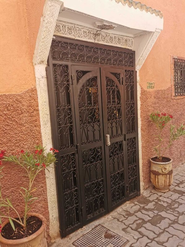 Une porte marocaine traditionnelle, ornée de motifs complexes en métal, flanquée de plantes en pot et bordée d’un chemin pavé.