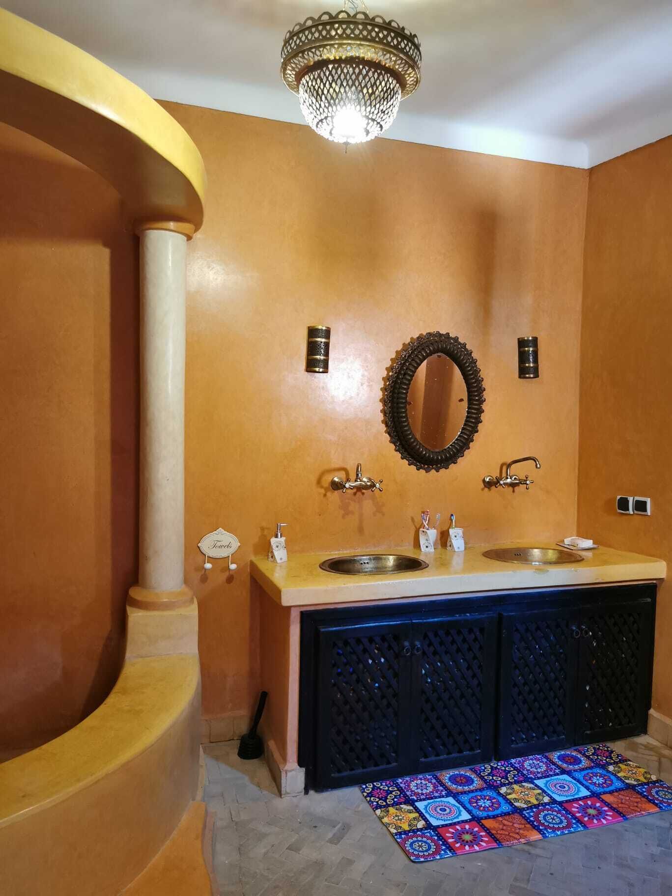 Une salle de bain avec un double lavabo, un miroir, un lustre et un tapis coloré.
