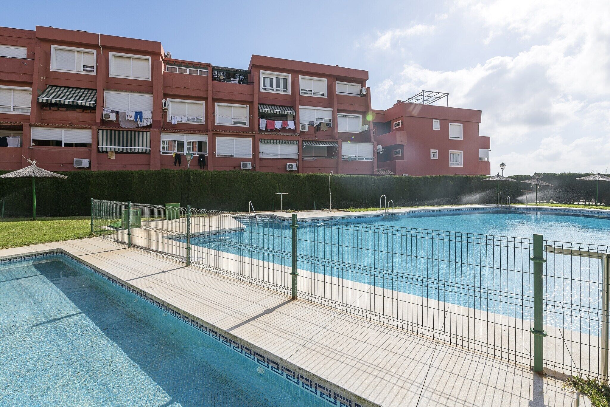 En swimmingpool med flisebelagt område, omgivet af et hegn i metal.
