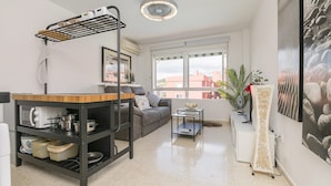 Un espacio habitable compacto con kitchenette, un sofá, una mesa de comedor y un ventanal con vistas a edificios.