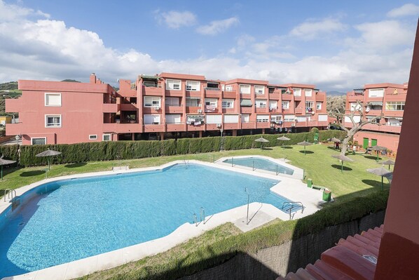 Una piscina rodeada por un césped cuidado y una hilera de edificios de apartamentos rosados.