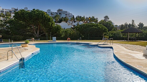 A swimming pool with a clear blue water, surrounded by a paved deck, a lifeguard chair, and a gazebo in the background. - Arte De Luz - Apartment In Calahonda-chaparral (Mijas (mÁlaga), Málaga)