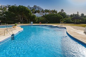 Ein Swimmingpool mit klarem, blauem Wasser, umgeben von einer gepflasterten Terrasse, einem Rettungsschwimmerstuhl und einem Gazebo im Hintergrund.